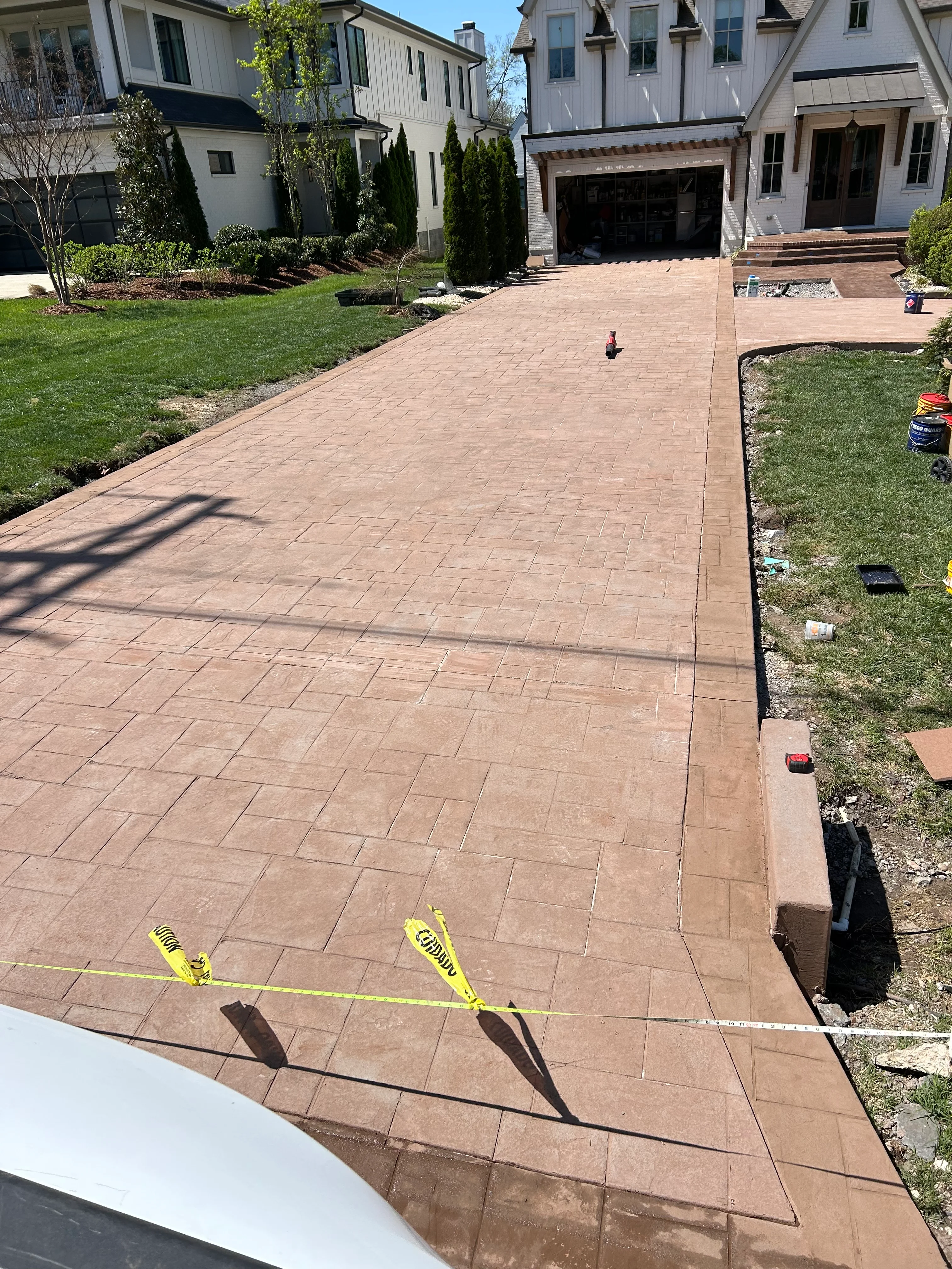 Newly installed terracotta concrete paver driveway with herringbone pattern in front of modern white farmhouse