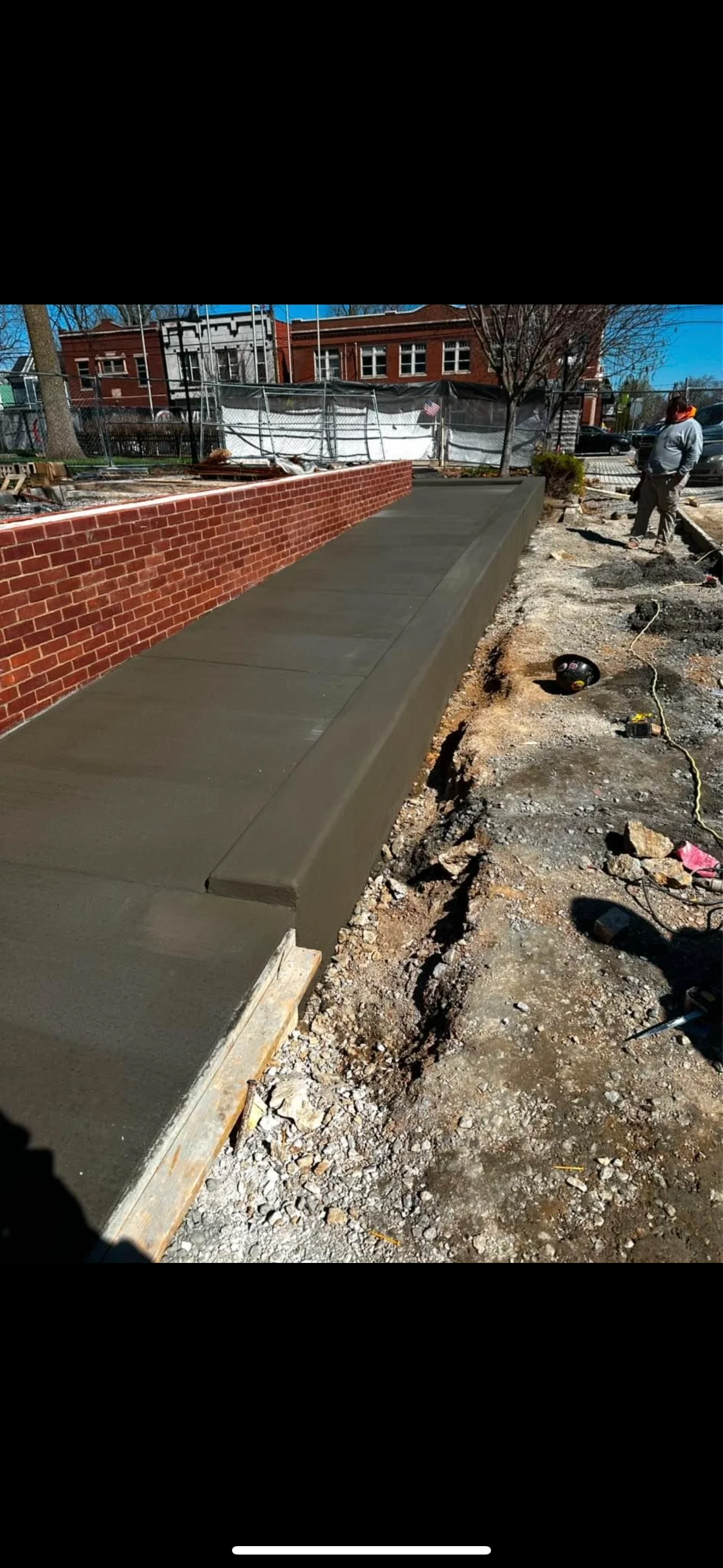 Freshly poured concrete walkway next to brick wall during construction in Lancaster