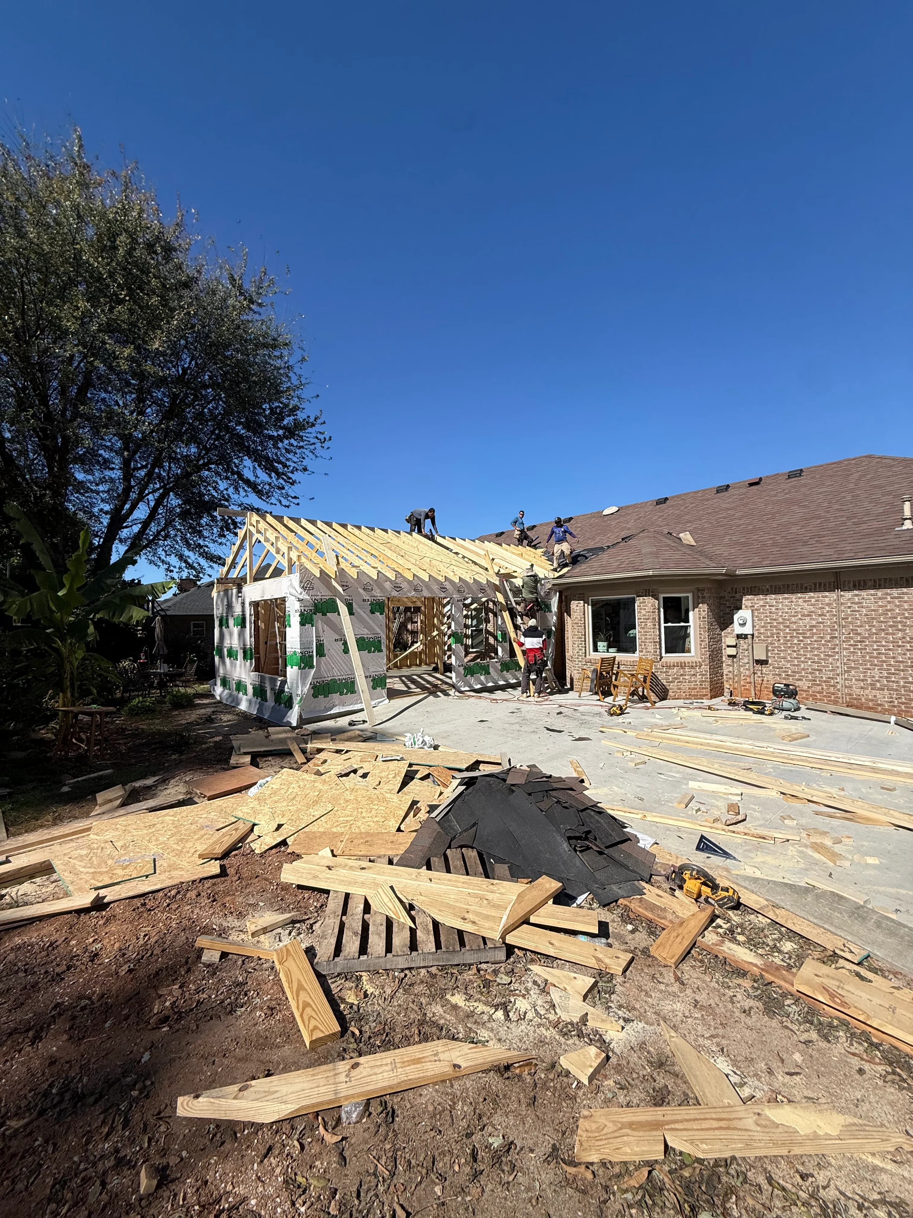 Residential home addition under construction with yellow framing and roof trusses exposed
