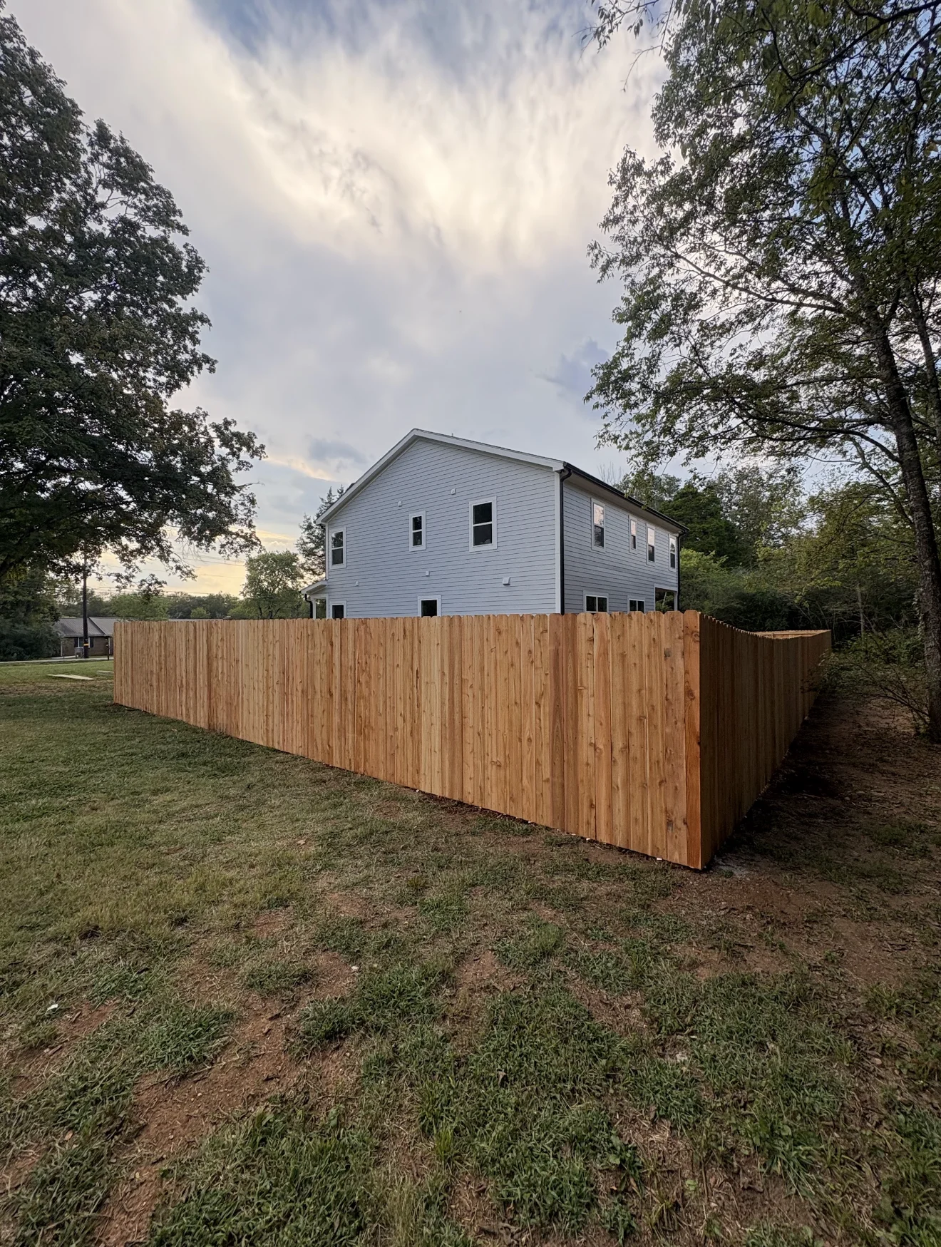 New wooden privacy fence installed around residential backyard with two-story house in background