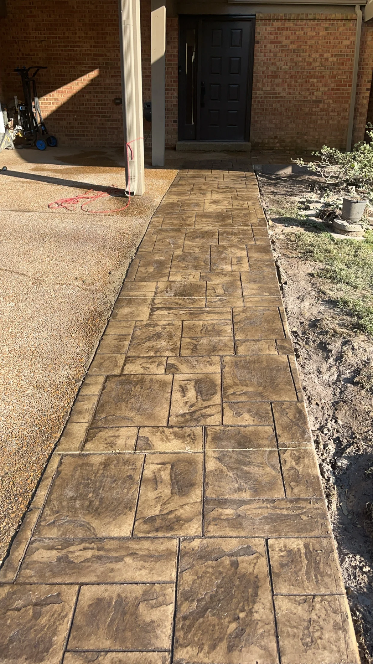 Stamped concrete walkway with ashlar slate pattern leading to black entry door